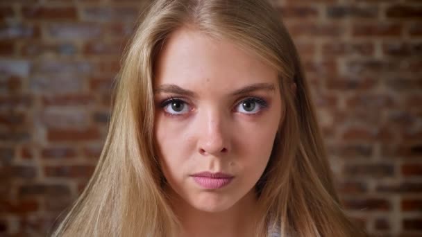 Jeune blonde caucasienne en colère regardant la caméra, portrait, mur de briques en arrière-plan — Video