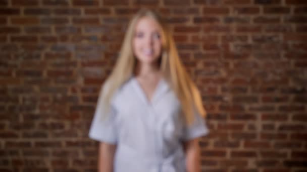 Concepto de atracción de enfoque. Joven chica rubia caucásica sonriendo y mirando a la cámara, retrato, pared de ladrillo en el fondo — Vídeos de Stock