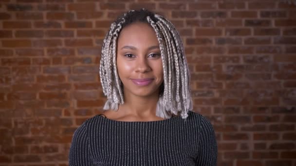 Young African girl with dreadlocks smiling and looking at camera, Brick wall in the background. — Stock Video