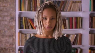 Genç Afrika ciddi kız gülümseyerek kameraya, dreadlocks kız ile kitap arka planda raflar
