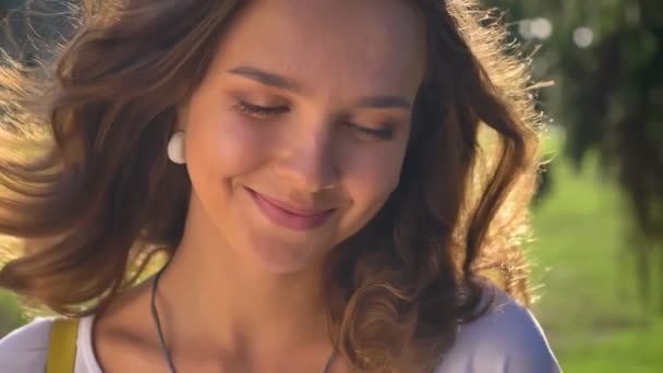 Porträtt av en ung leende, blyg kaukasiska brunett i parken, universitet i bakgrunden — Stockvideo