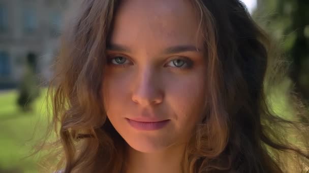 Porträt einer jungen lächelnden, lachenden kaukasischen Brünette im Park, Universität im Hintergrund — Stockvideo