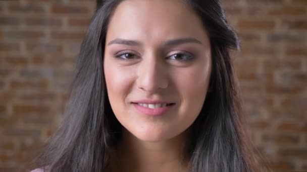 Portré egy fiatal, magabiztos mulatto lány nézett a kamerába, és mosolyog, a háttérben egy téglafal — Stock videók
