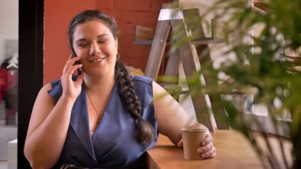 Blubber modelo caucásico hablando por teléfono y respondiendo con emociones felices y beber café — Vídeos de Stock