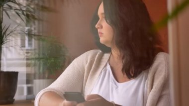 Fubsy gülen beyaz kız Vitrinlere bakıyor ve Smartphone'da yazarak holding