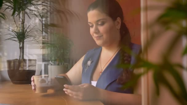 Heavy nice caucasian woman holding her planshet and scrolling while drinking coffee beside window — Stock Video