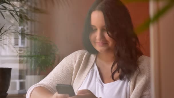 Велика концентрована біла дівчина тримає планшет і друкує в кафе — стокове відео