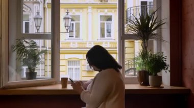 Şişman beyaz kadınları kağıt bardak kafe penceresinde yakınındaki cep telefonunda kaydırma