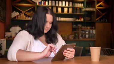Planshet kapalı masada büyük kağıt bardak ile konsantrasyon ile swiping obez beyaz kız