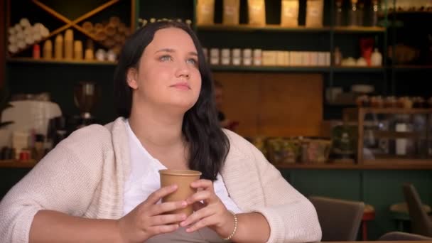 Большая мечтательная белая женщина думает и держит свой напиток в кафе — стоковое видео