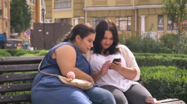Smartphone ve typying açık bankta otururken birlikte bakarak iki obez beyaz kız