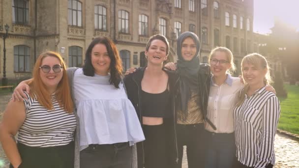 Разнообразная группа смеющихся кавказских девушек, стоящих рядом и держащих с гордостью на улице днем — стоковое видео