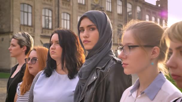 Joven mujer caucásica en hijab directamente entre otras diversas chicas en línea fuera — Vídeo de stock