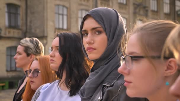 Gorgeous caucasian girl in hijab looks precisely from group of various women outdoor — Stock Video