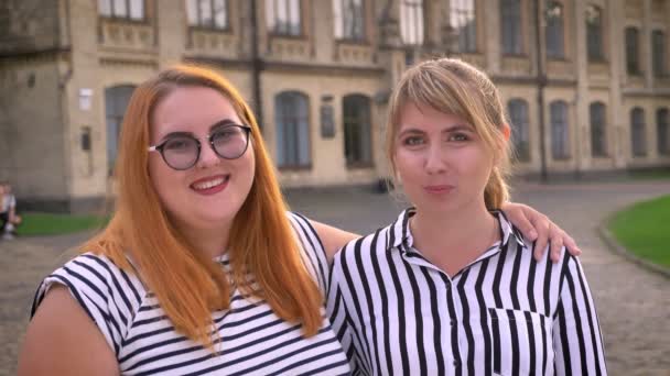 Stout Kaukasische meisje lachen met haar dunne vriendin terwijl knuffelen buiten met glimlach — Stockvideo