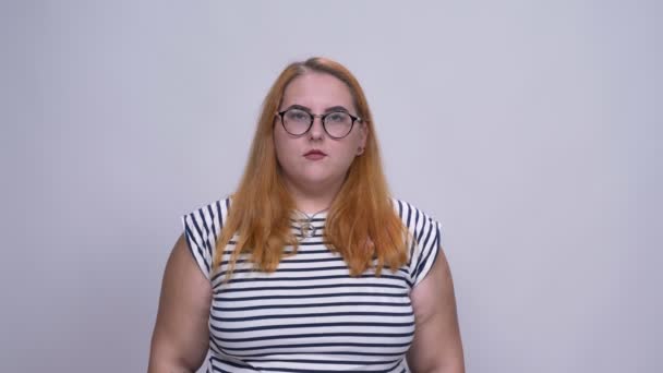 Obézní kavkazské rusovlasá dívka ukazuje znamení moci s jistotou stálého přední šedé pozadí uvnitř — Stock video