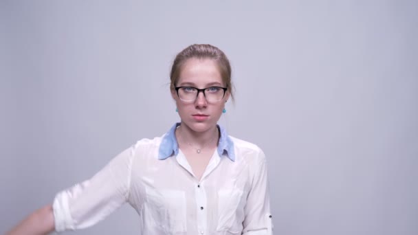 Симпатична біла дівчина показує силовий знак зосереджений з серйозним обличчям на сірому фоні — стокове відео