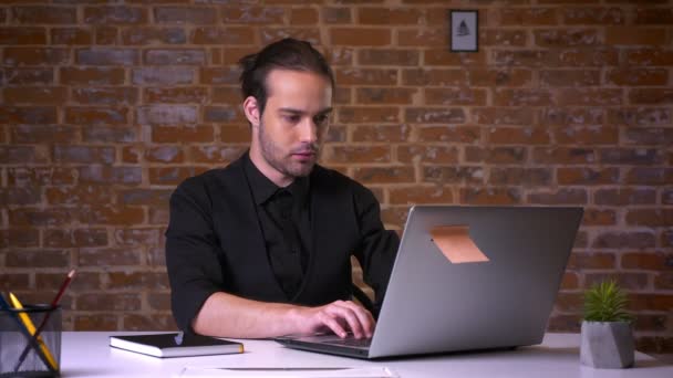 英俊的高加索男性停止工作的笔记本电脑惊讶和困惑的脸, 看着相机, 而坐在砖工作室 — 图库视频影像