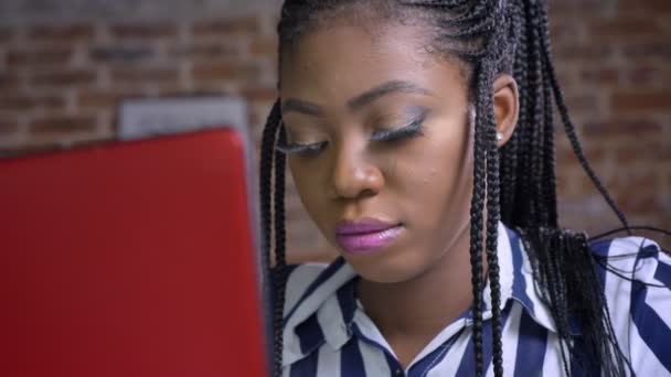 Красивая африканская модель смотрит на красный ноутбук и печатает с уверенностью и концентрацией — стоковое видео