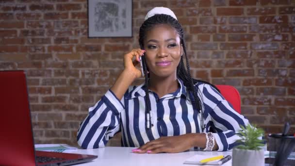 Beszélő afrikai lány, aki fosuced a telefon beszélgetés nyugodt ülve piros stúdió — Stock videók