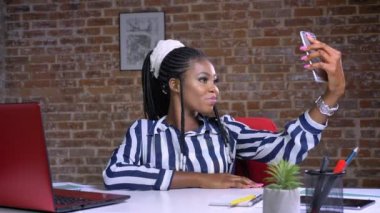 Selfie alma ve onun işyerinde kırmızı ofiste otururken gülümseyen güzel Afrikalı kız