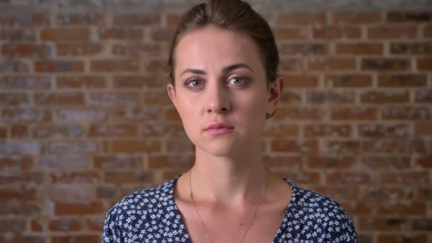 Концентрированная брюнетка кавказская девушка смотрит в камеру с уверенностью стоя возле кирпичной стены — стоковое видео