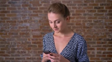 güzel esmer beyaz kız onu smartphone değnek ayakta kırmızı tuğla duvar rahat ve sakin yakınındaki kaydırma