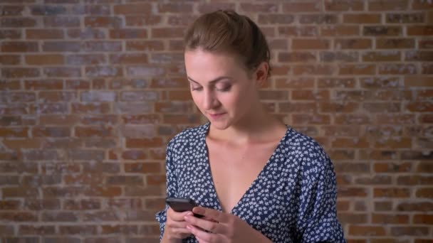 Fin Brunett kaukasiska tjej rullning hennes smartphone wand stående nära röd tegelvägg avslappnad och lugn — Stockvideo