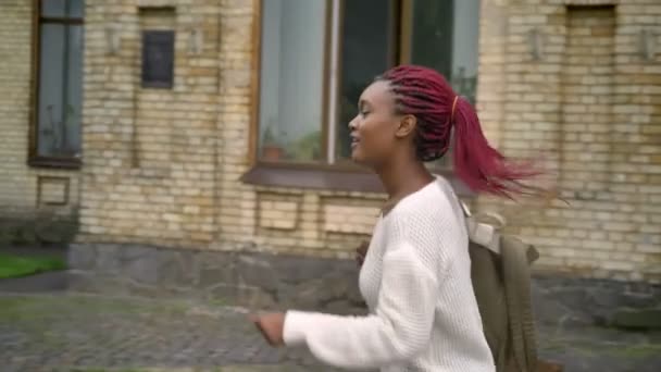 Joven mujer africana encantadora huyendo de la universidad, estudiante con mochila y rastas rosadas — Vídeo de stock