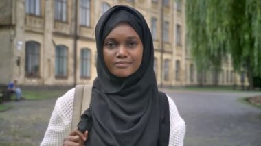 Sırt çantası tutarak ve kamera, üniversite Parkı ayakta gülümseyen hijab genç Müslüman Afrika öğrenci