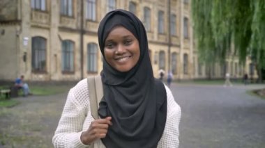 Kameraya gülümseyen ve sırt çantası, üniversite Parkı ayakta tutan hijab güzel Afrikalı-Amerikalı Müslüman kadın