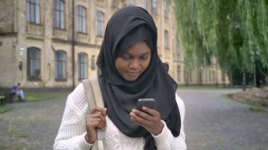 Genç Afrika Müslüman kız öğrenci telefona yazma ve üniversite Parkı ayakta hijab içinde