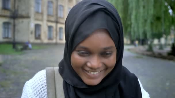 Afrikaanse jonge moslimvrouw in hijab lachen in de camera en permanent in park in de buurt van Universiteit, gelukkig en vrolijk — Stockvideo