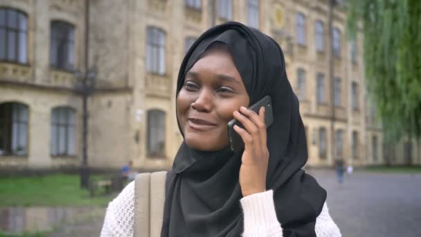 年轻的非洲穆斯林妇女在盖头交谈电话和微笑 站在公园附近的大学 快乐和开朗 — 图库视频影像