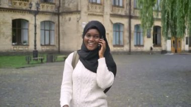 Güzel Müslüman Afro-Amerikan kız öğrencinin Üniversite uzak yürüme ve cep telefonuyla konuşan hijab içinde