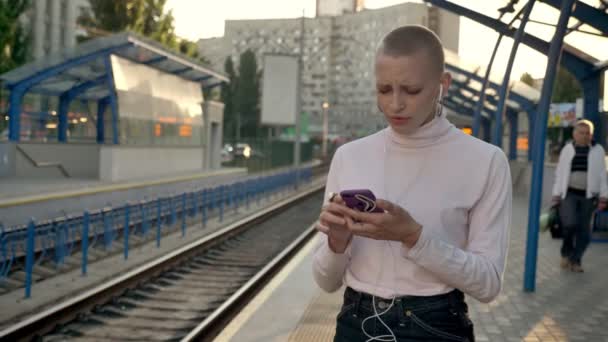 Gyönyörű kaukázusi kopasz nő, a vasútállomás mellett hallgató-hoz zene szabadtéri mozgás — Stock videók