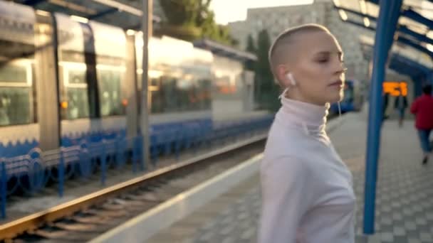 Unusual dance of young bald caucasian girl on platform with train behind her in summertime — Stock Video