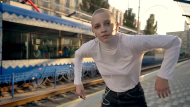 Moderna chica calva bailando se está moviendo en la estación de tren de pie en la plataforma exterior en verano — Vídeo de stock