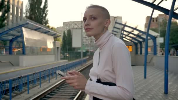 Young nice caucasian female swiping tablet and listening to music at railway station in summer — Stock Video