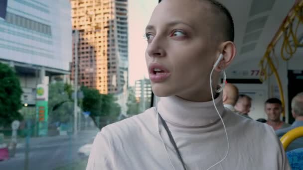 Triste extraordinaire fille caucasienne chante avec joie dans les écouteurs tout en étant assis près de la fenêtre dans les transports en commun, vue sur la ville — Video