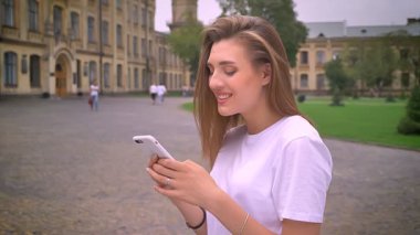 korku veren beyaz kız telefonunu sokakta sakin ve cezalandırmak, kentsel odaklı profilde dururken kaydırma