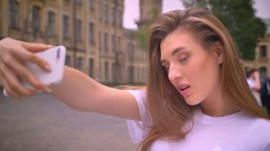 Yalnız güzel beyaz kız ayakta yakın kamera ve alma selfie ile odaklı kentsel arka yüzüne yakın çekim