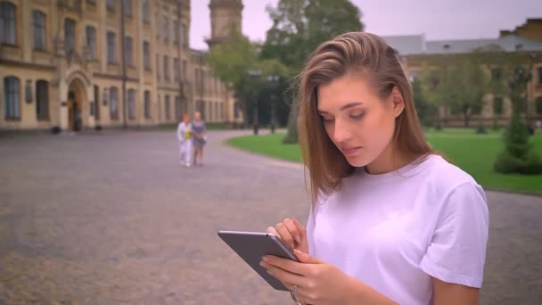 Bonito loira caucasiana fêmea deslizando seu tablet na rua calma e relaxada, de pé na área urbana, durante o dia — Vídeo de Stock