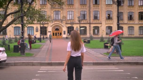 Silhouette concentrée de belle fille caucasienne, marchant vers l'ancien bâtiment, traversant la route, se déplaçant rapidement dans la ville — Video