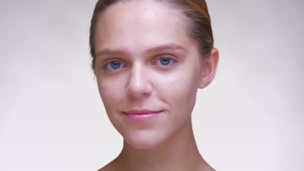 Close-up sorridente rosto de menina branca bonito com pele clara e olhar aberto no fundo branco — Vídeo de Stock