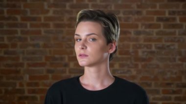 Mutlu beyaz sarışın kadın kamera kapalı tuğla duvarın yanında kalmasından ve tüyler ürpertici odaklanmıştır