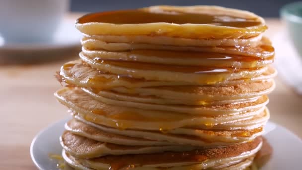 Смачні свіжі млинці, які чекають, коли їх з'їдять на столі, використовуються з таненням золотого меду на дерев'яній поверхні — стокове відео