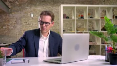 Masada oturan ve yalnız office ve içme suyu içinde laptop çalışan yakışıklı beyaz iş adamı