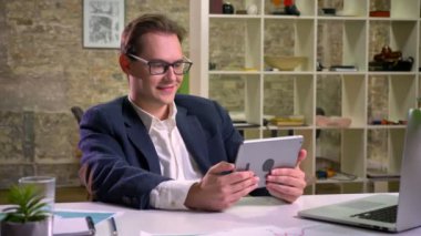 Onun tablet ve zevk ile waching tutan mutlu beyaz işadamı laptop kapalı yakınındaki masada otururken konsantre