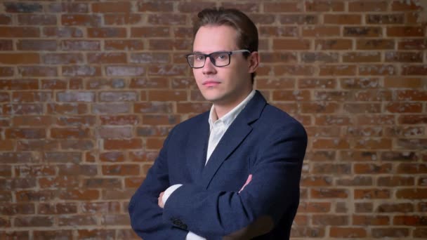 Caucasian office worker standing seriously with his hands crossed near brick wall, serious mood — Stock Video